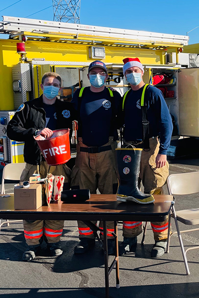 Volunteers posing with fundraiser buckets and fire truck in background 